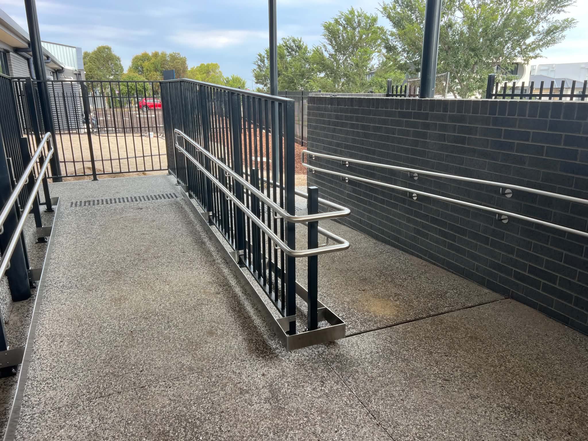 Stainless steel handrails and black balustrades along an outdoor accessible ramp